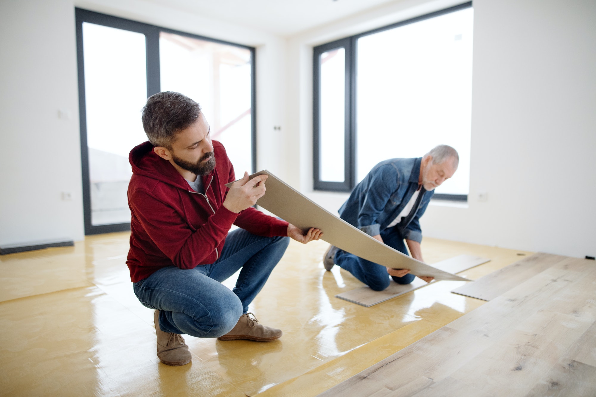 A mature man with his senior father laying vinyl flooring, a new home concept.